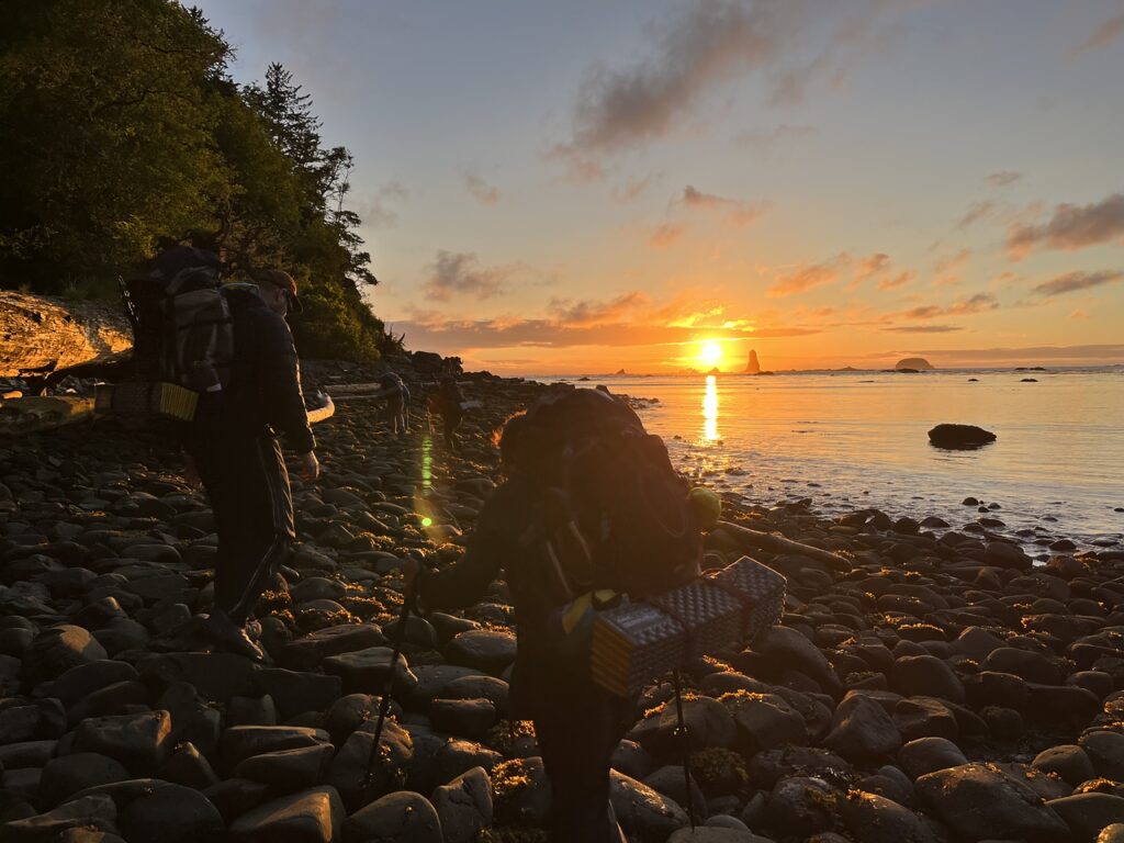 Ŷĳs hiking on rocks along the beach at sunset