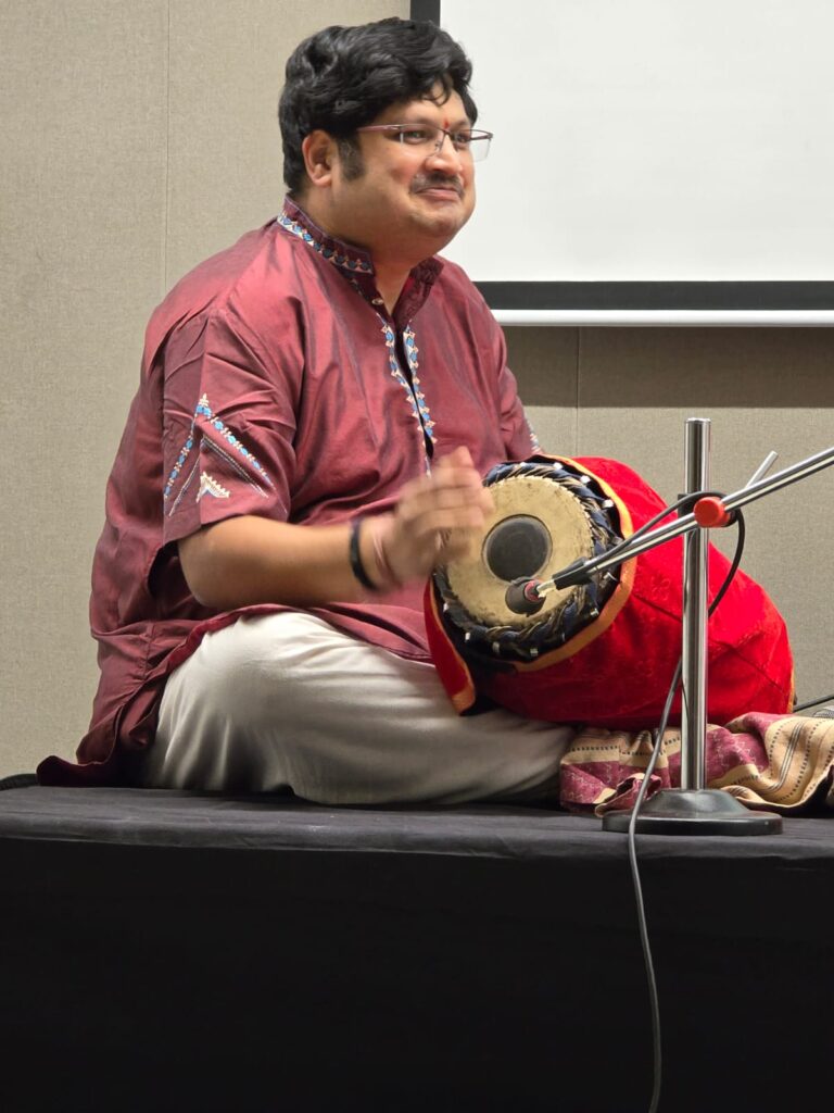 A classic Indian music performer sitting on stage and playing a drum